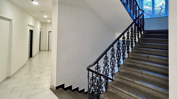 Un interior moderno con una escalera, paredes blancas y suelo de baldosas.