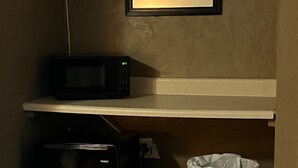 A compact kitchen with a microwave, a small refrigerator, and a trash bin. - The Travelers Inn (Jacksonville)