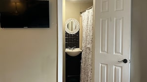 A bathroom with a white door, a black sink, a mirror with a decorative frame, and a television mounted on the wall. - The Travelers Inn (Jacksonville)