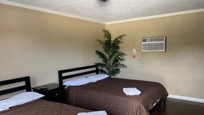 A hotel room with two beds, a nightstand, a potted plant, and an air conditioning unit. - The Travelers Inn (Jacksonville)