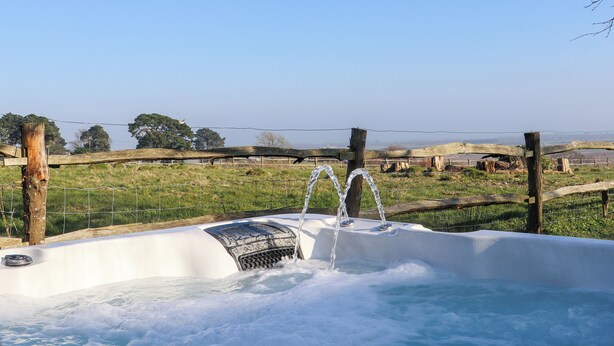 Un jacuzzi con vistas despejadas del paisaje circundante, que incluye una valla de madera y árboles al fondo.