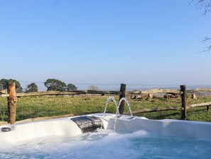 A hot tub with a clear view of the surrounding landscape, including a wooden fence and trees in the background. - Birch Cottage (Rye)