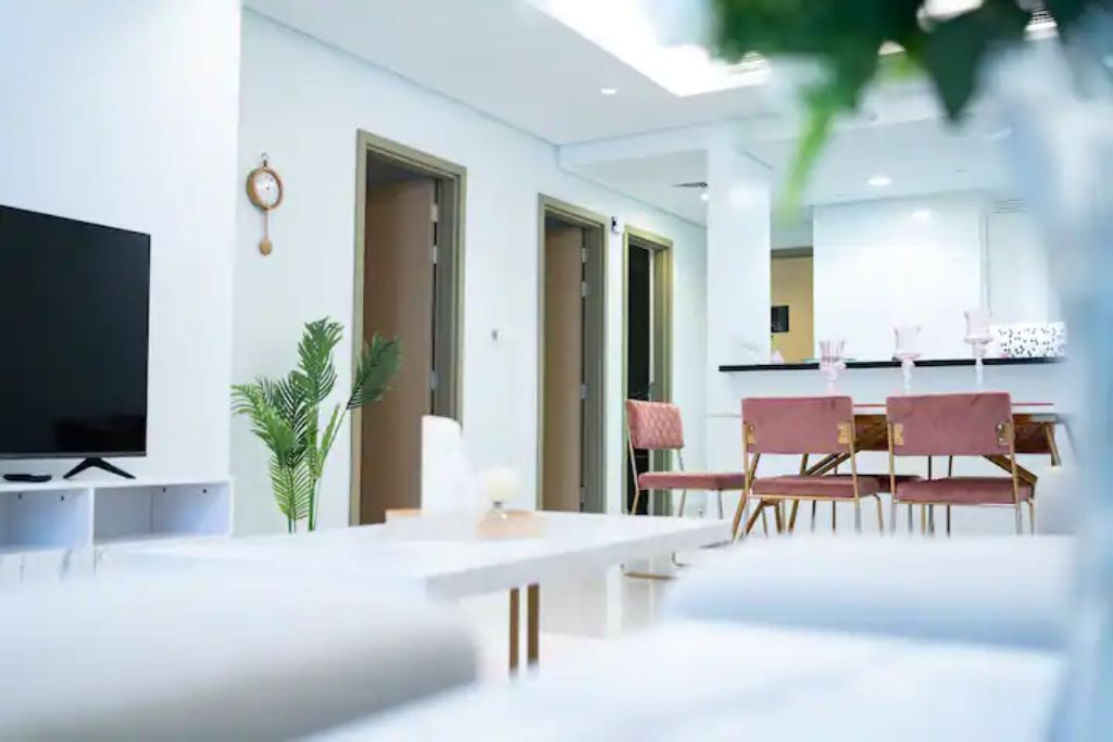 Una sala de estar moderna con un televisor de pantalla plana, un comedor con sillas rosadas y un ventanal grande.