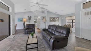 A spacious living room with a large leather sofa, a coffee table, and a ceiling fan.