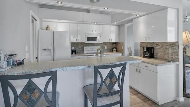 A modern kitchen with white cabinetry, a central island with bar stools, a microwave, and a coffee maker.