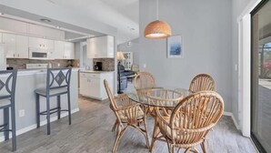 A modern kitchen with white cabinets, a central island with bar stools, and a dining area with wicker chairs and a glass table.