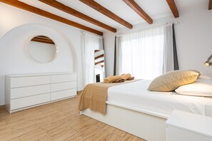 A bedroom with a bed, a white wardrobe, a round mirror, and wooden beams on the ceiling.