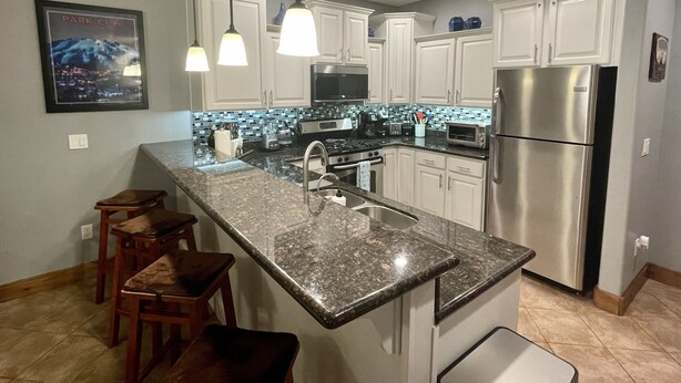 Cozinha moderna com bancadas de granito, eletrodomésticos de aço inoxidável e iluminação pendente.