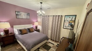 Um quarto com cama, mesas de cabeceira, um candelabro, um quadro e um cartaz na parede.