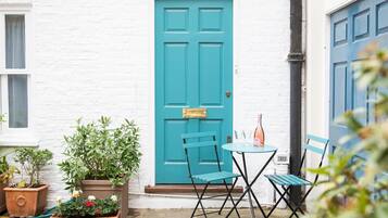 A white brick building with a turquoise door, a small table with chairs, and potted plants.