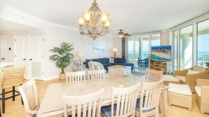 Een ruime woonkamer met een grote eettafel, comfortabele zithoek, een kroonluchter en een balkon met uitzicht.