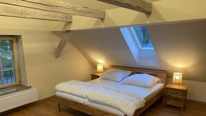 A bedroom with a sloped ceiling, a skylight, a wooden bed, two bedside tables with lamps, and a radiator.