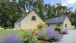 A stone building with a sloped roof, surrounded by a well-maintained lawn and flowering plants.