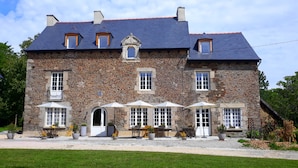 A stone building with multiple windows, a central entrance, and outdoor seating with umbrellas. - Le Manoir des Haies (Les Champs-Geraux)