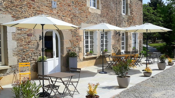 An outdoor seating area with tables and chairs, umbrellas, and potted plants. - Le Manoir des Haies (Les Champs-Geraux)