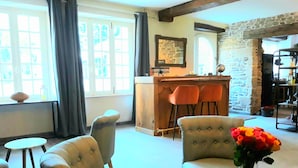 A cozy living room with a bar area, featuring two armchairs, a round table, and a vase of flowers. - Le Manoir des Haies (Les Champs-Geraux)