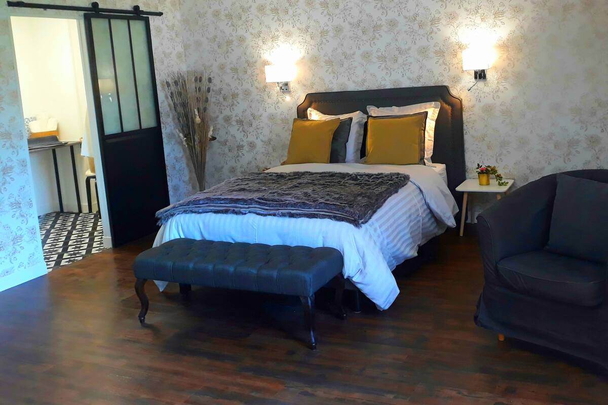 Une chambre à coucher avec un lit, un banc, une chaise et une petite table sur laquelle est posée une plante.