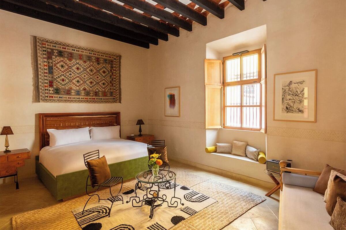 Un dormitorio con una cama grande, una ventana con vistas, techo de madera y alfombra estampada.