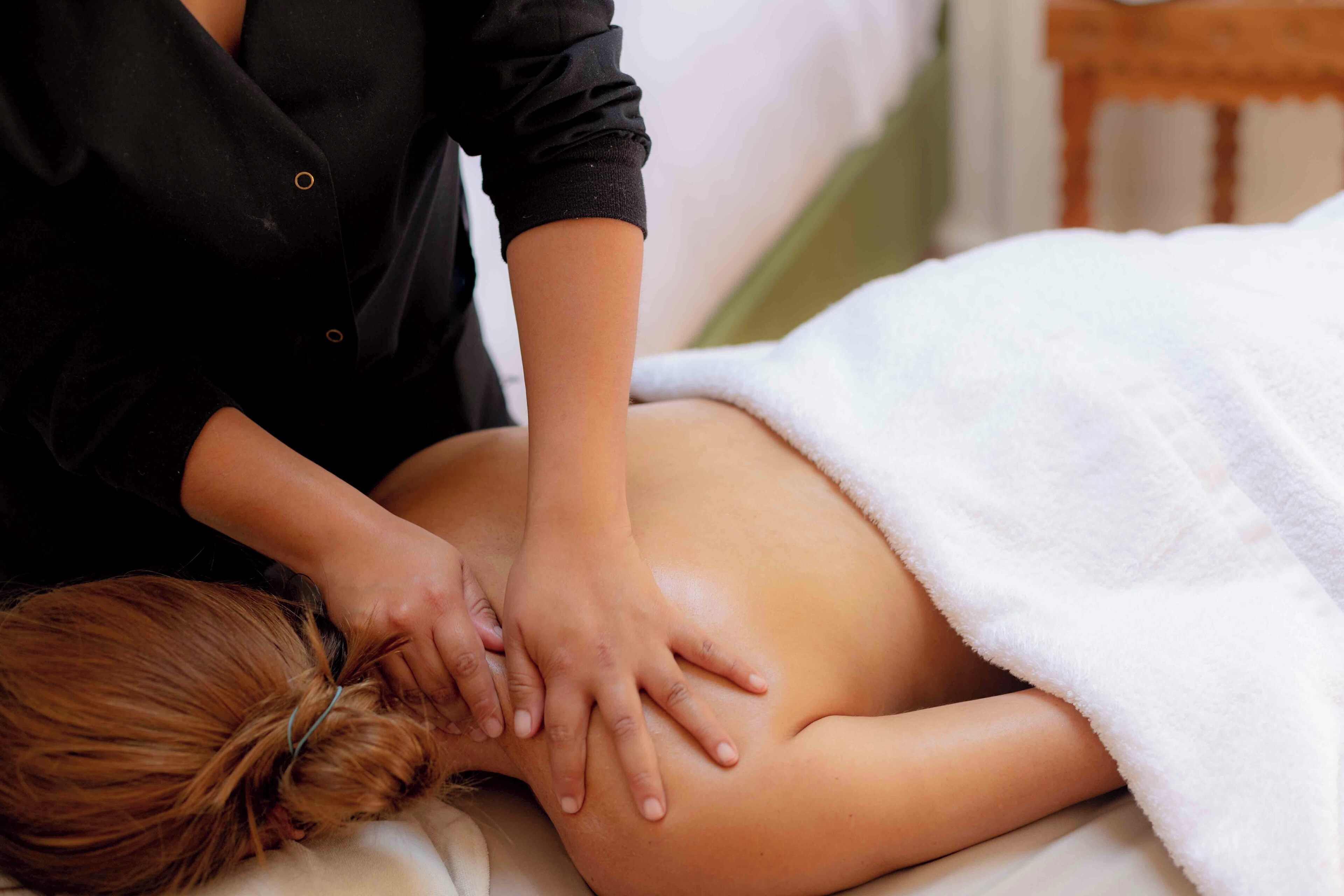 A person receiving a back massage in a room with a bed and a wooden chair.