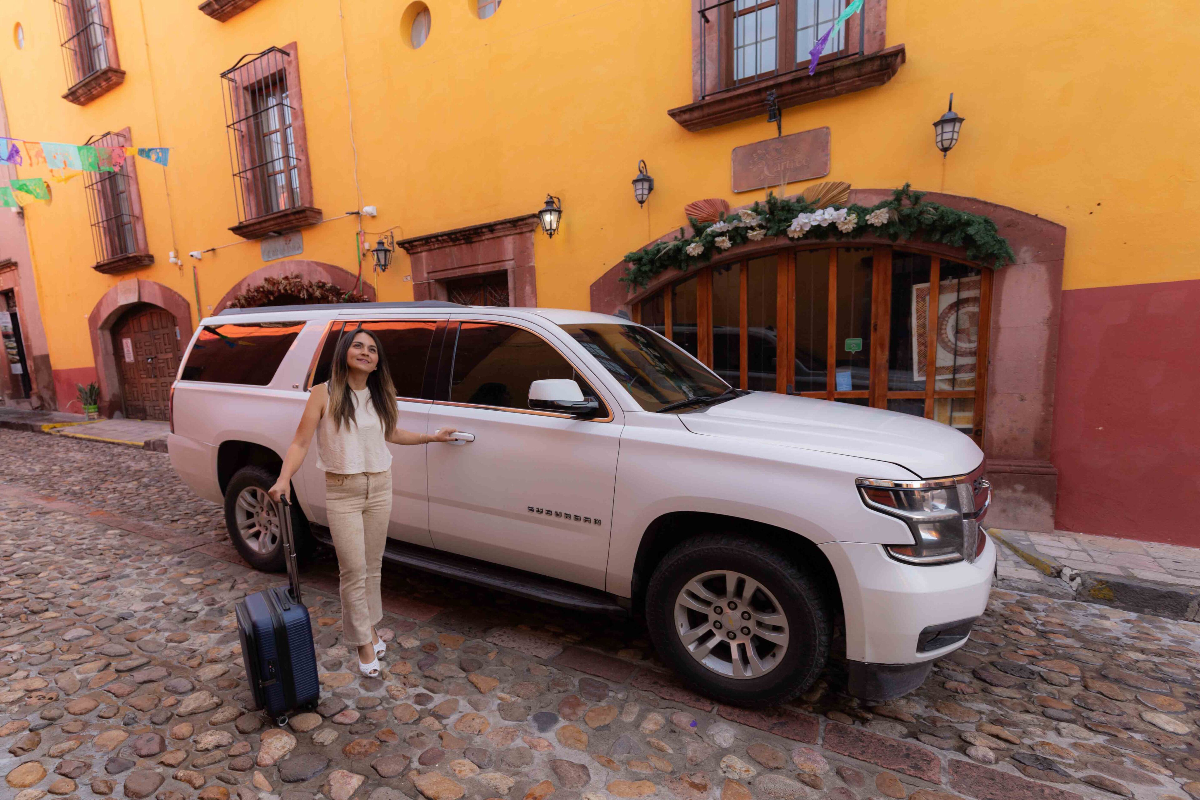 A white SUV parked on a cobblestone street in front of a yellow building with a wooden door and windows.