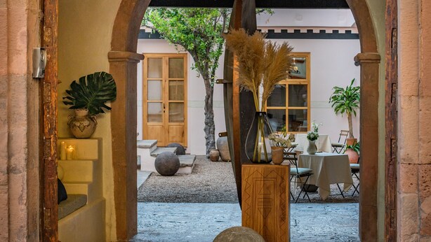 An arched doorway leading to a courtyard with a chandelier, potted plants, and a rustic stone bench. - La Valise San Miguel de Allende, Member of Small Luxury Hotels (San Miguel de Allende)