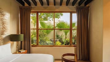 Habitación de hotel con una ventana grande, una cama, una silla y una mesita de noche con lámpara.