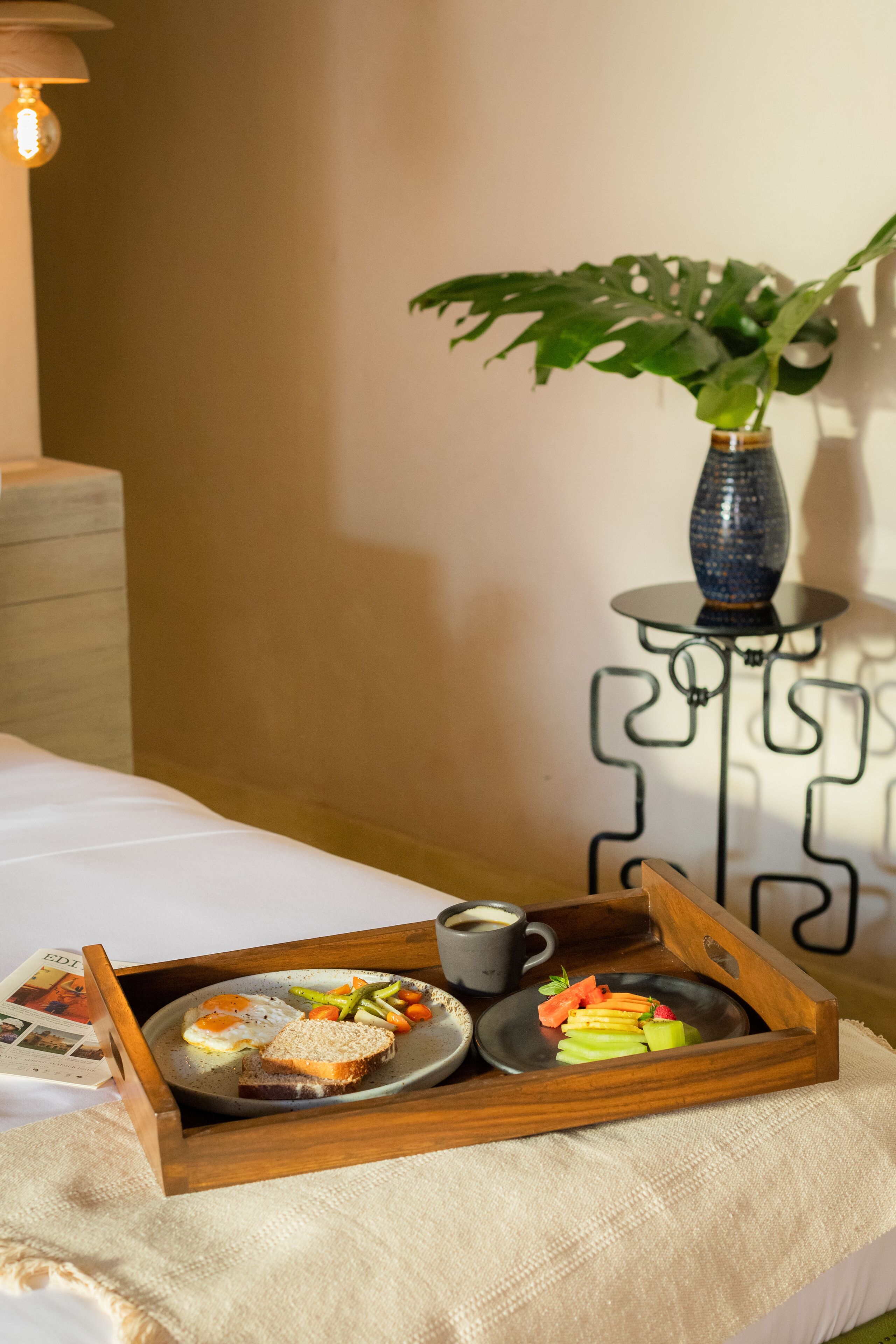 Bandeja de desayuno con tostadas, huevos, verduras y una taza sobre la cama.