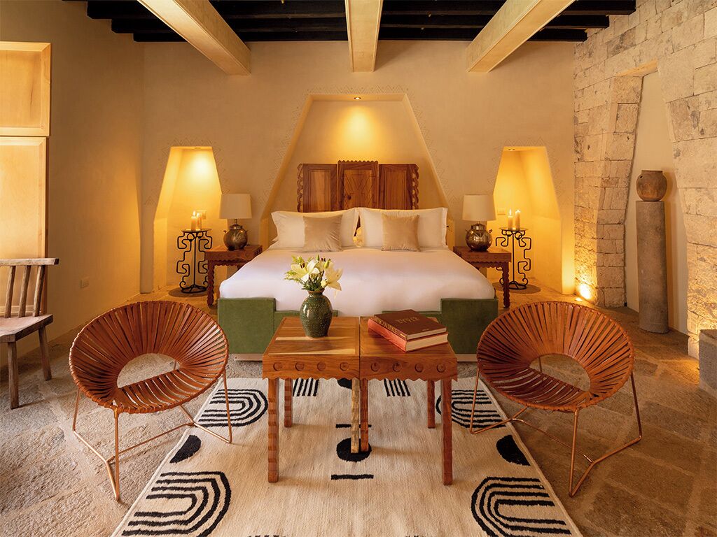 A bedroom with a bed, two lamps, a table with books, and two chairs.