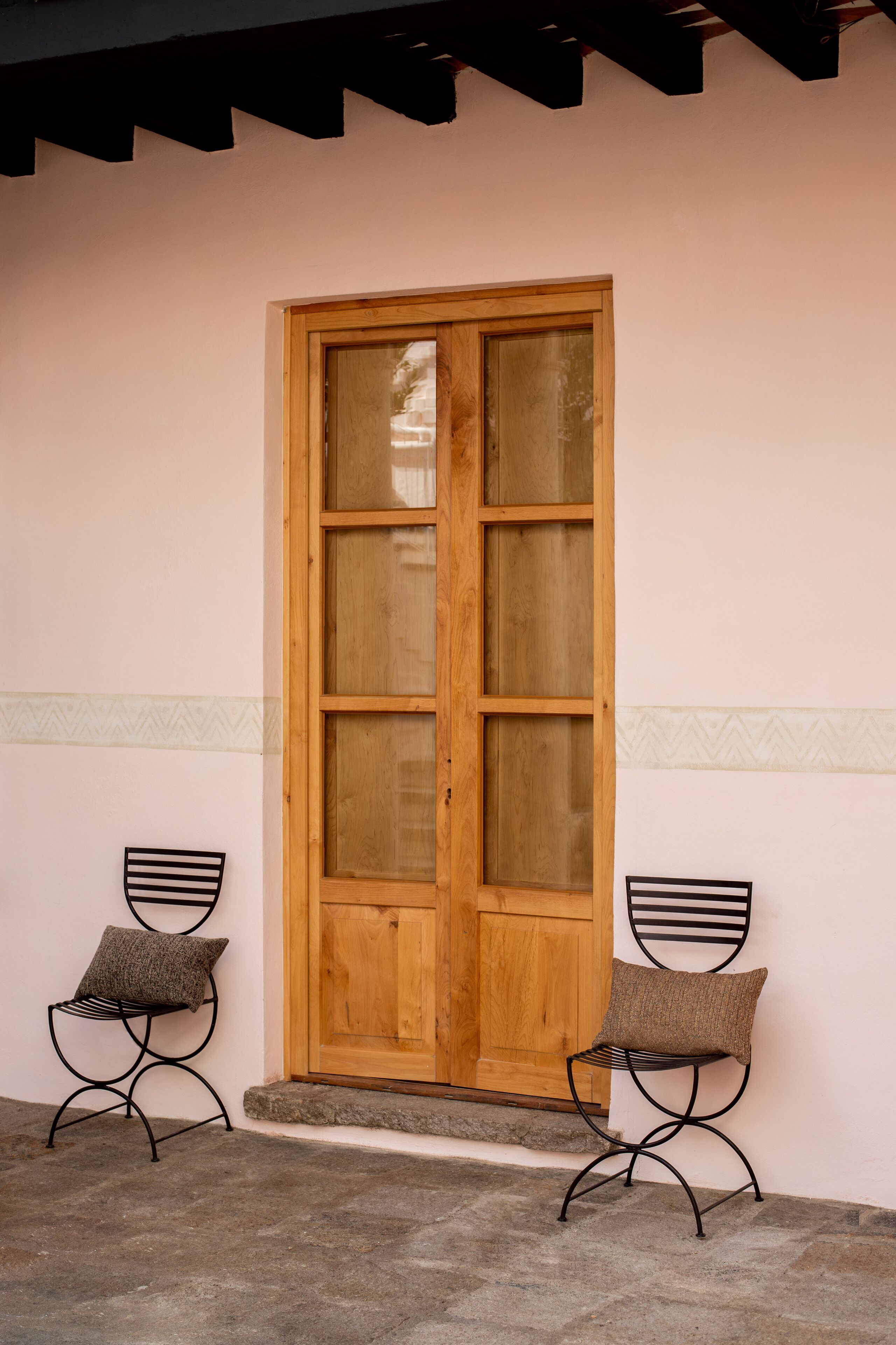 A wooden door with glass panels, flanked by two metal chairs with cushions.