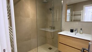 Un baño moderno con ducha acristalada, lavamanos blanco y tocador de madera.
