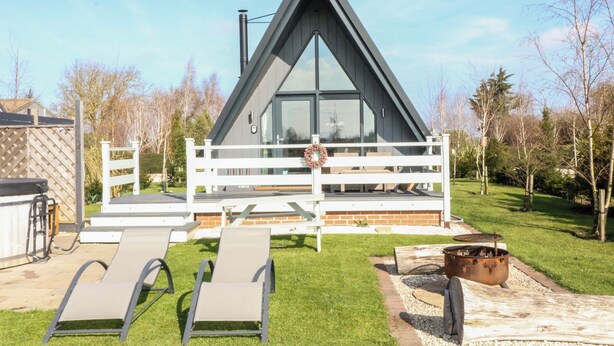 Ein modernes Haus mit einem dreieckigen Dach, einer Terrasse mit Liegestühlen und einem Grillbereich.