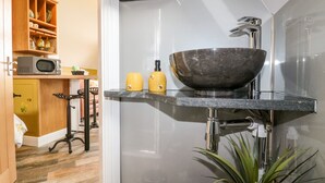 Ein modernes Badezimmer mit einem großzügigen Vessel-Waschbecken, einer Mikrowelle und einem kleinen Regal mit Dekoration.