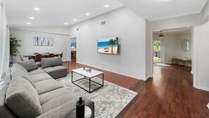 A spacious living room with a large sectional sofa, a coffee table, and a painting of a beach scene. - 15 Mins to Beach! Safe & Quiet Home Near Beach & Downtown~Heated Pool~Ping Pong/Foosball. (Fort Lauderdale)