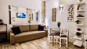 Moderni olohuone, jossa on ruskea sohva, valkoiset tuolit, lasinen ruokapöytä ja seinälle asennettu televisio.