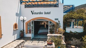 L'ingresso dell'hotel Venardos, con un letto visibile all'interno, gradini in pietra e piante in vaso.