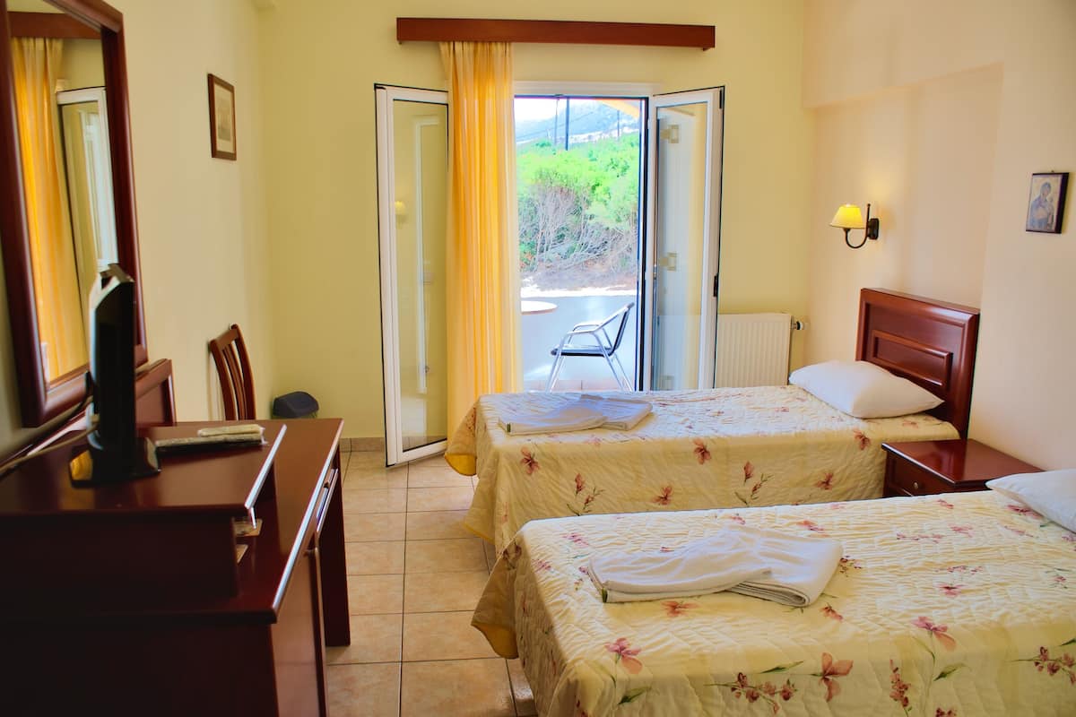 A hotel room with two beds, a desk, a chair, and a view of the outdoors through a sliding door.