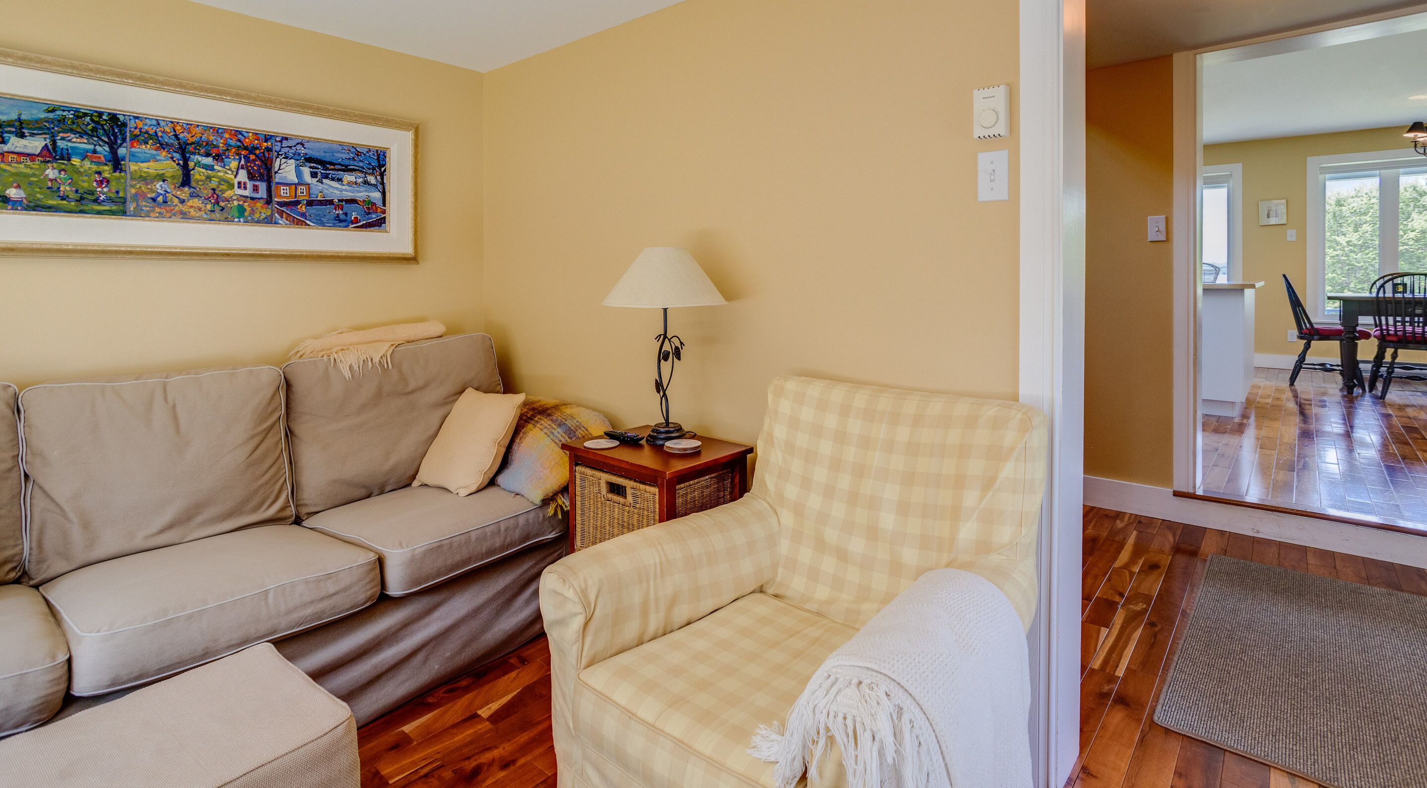 Una sala de estar con un sofá color beige, un sillón a cuadros, una mesita con una lámpara y un cuadro enmarcado en la pared.