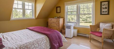 Un dormitorio con cama, cómoda, silla y dos ventanas.