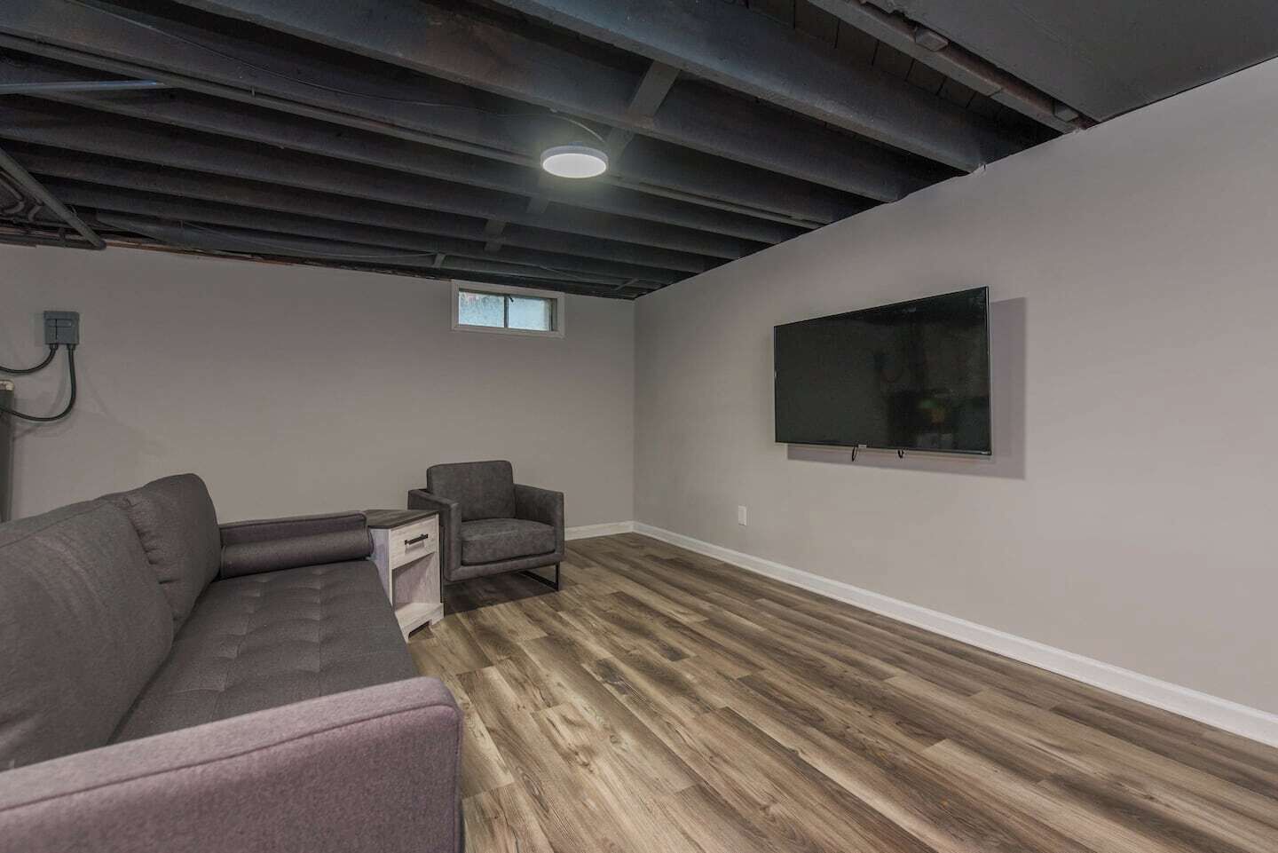 Una habitación con sofá modular, una silla, un televisor montado en la pared y piso de madera.