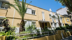 Um edifício amarelo com molduras de janela brancas, uma varanda e uma palmeira em primeiro plano.
