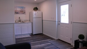 A compact kitchen with white cabinetry, a refrigerator, and a window with a view of the outdoors. - Beautiful new property, great location. (Waves)