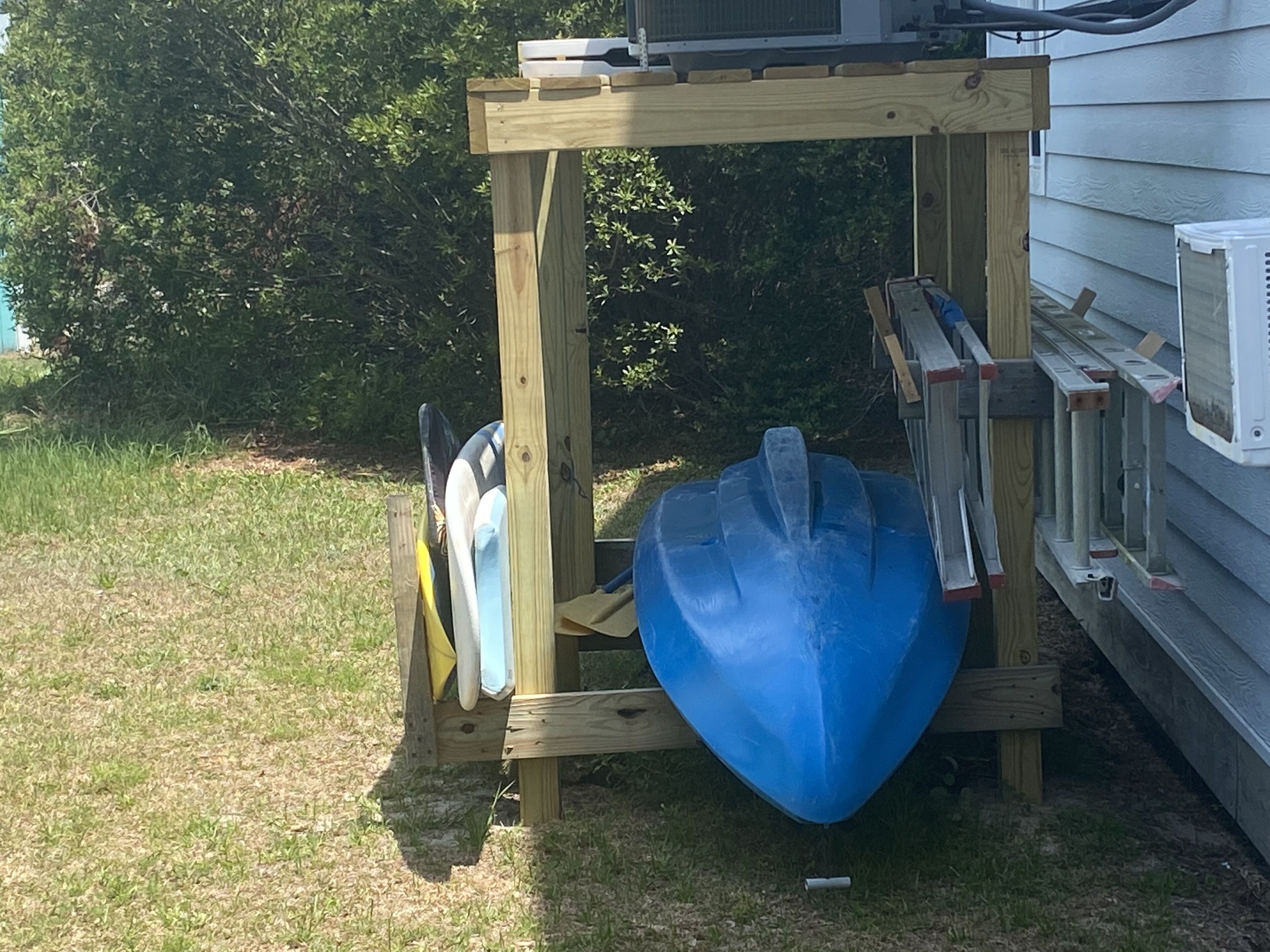 A wooden structure with a blue object hanging from it, possibly a kayak or paddleboard, and a ladder attached to the side.