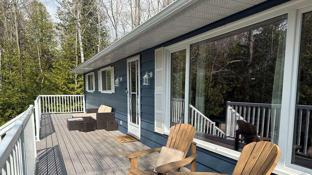 A wooden deck with outdoor furniture, including two chairs and a table, and a covered area with a railing.