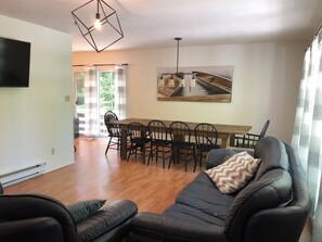 Uma sala de estar moderna com um sofá de couro preto, uma área de jantar com mesa e cadeiras de madeira, e uma pintura grande na parede.