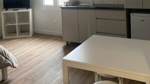 A compact kitchen with a window, a small table, and a television on a stand. - Location Vignerons (Neuvy-sur-Loire)