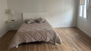 A bedroom with a bed, a nightstand, a lamp, and a window. - Location Vignerons (Neuvy-sur-Loire)