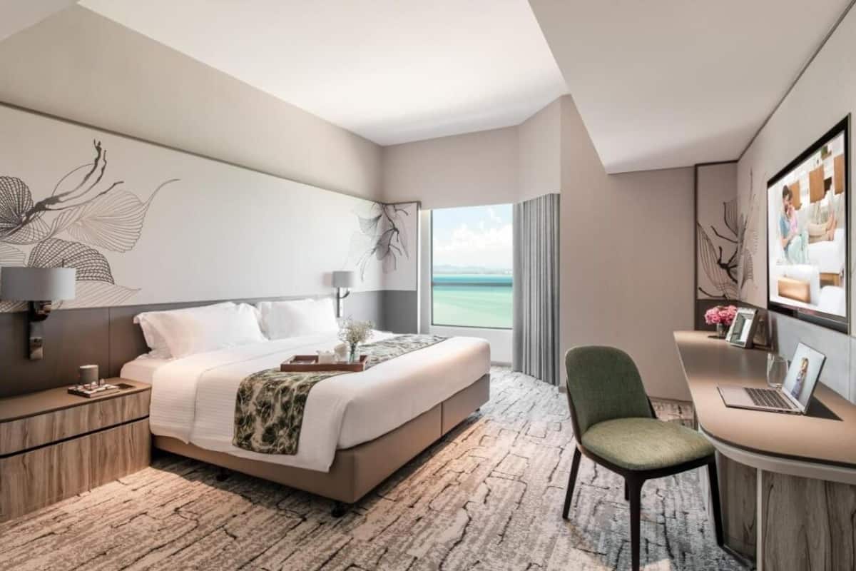 Habitación de hotel moderna con una cama grande, un escritorio con una computadora portátil, una silla y vista al mar.