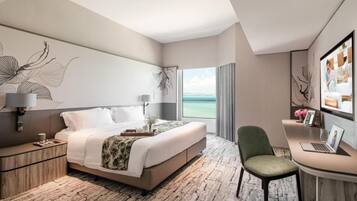 A modern hotel room with a large bed, a desk with a laptop, a chair, and a view of the sea.