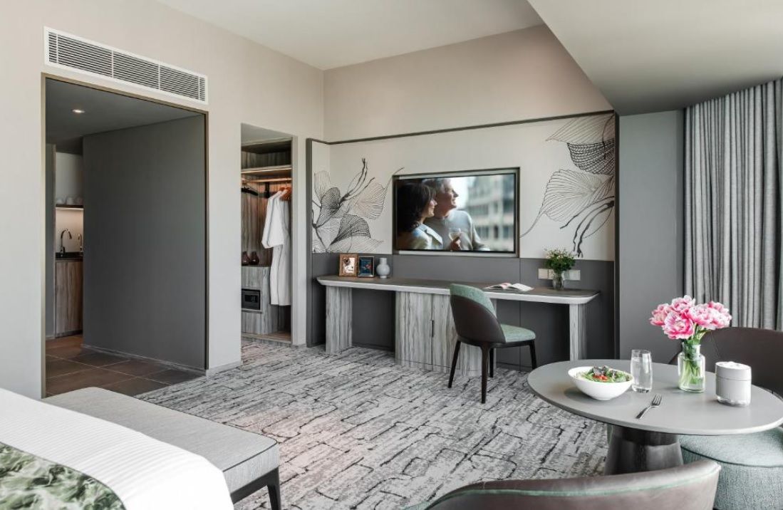 A modern hotel room with a dining area, a TV mounted on the wall, and a visible closet.