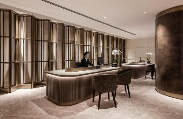 A reception desk with a modern design, a large pillar, and a seating area with chairs.